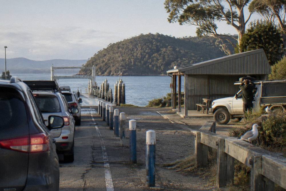 Cars queued in lanes at a ferry terminal waiting to board a vessel on a calm morning