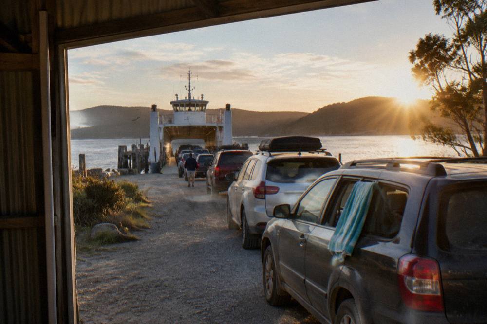 Cars queued in a line at a small ferry terminal beside a sheltered bay