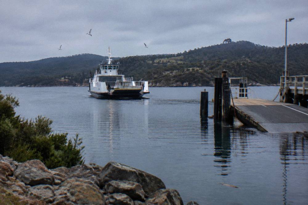 A vehicle ferry approaching a timber ramp at a small island terminal in flat evening light