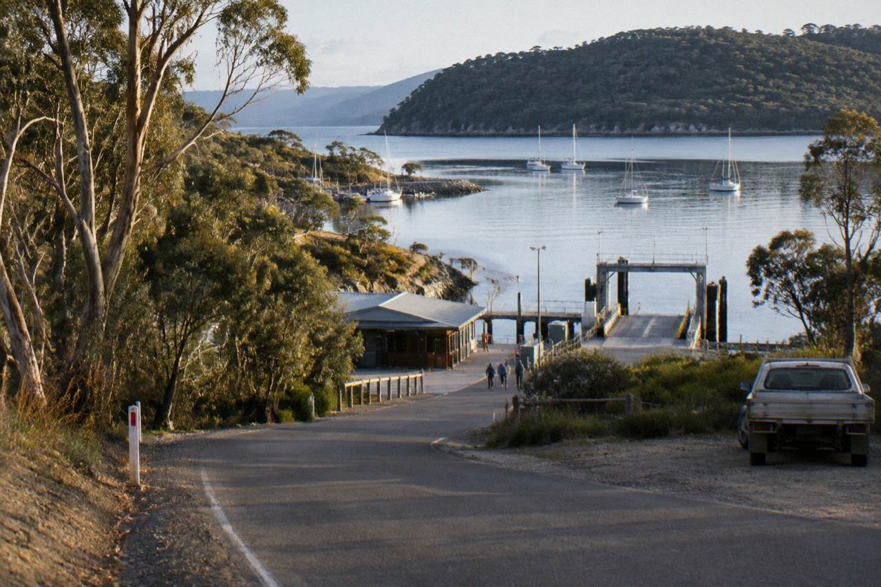 A quiet country road winding toward the Kettering marina with yachts moored on still water