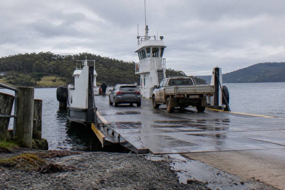 Ferry ramp lowered onto a shoreline with vehicles boarding in daylight