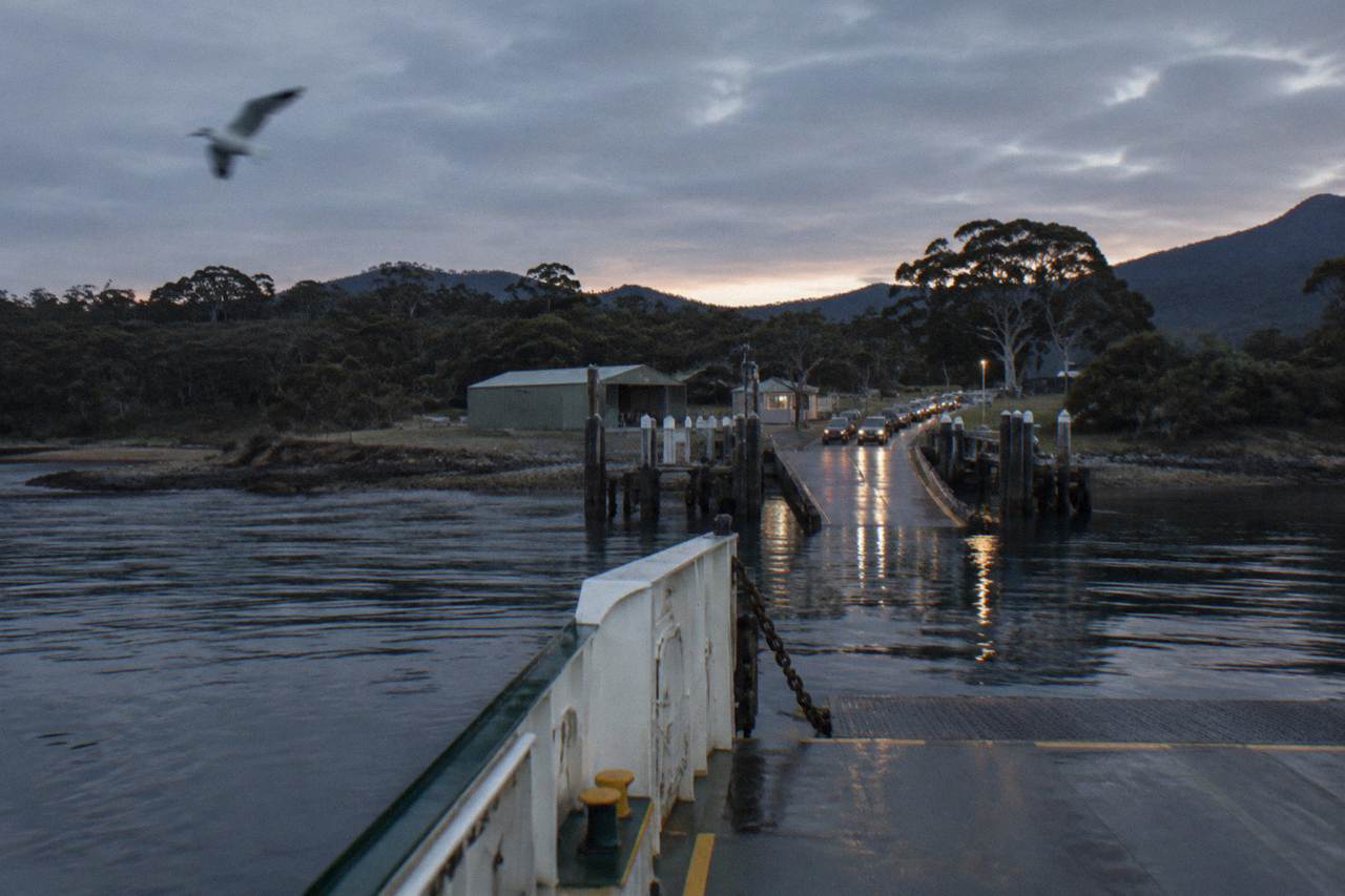 Vehicle ferry approaching a small jetty terminal across calm water at dusk