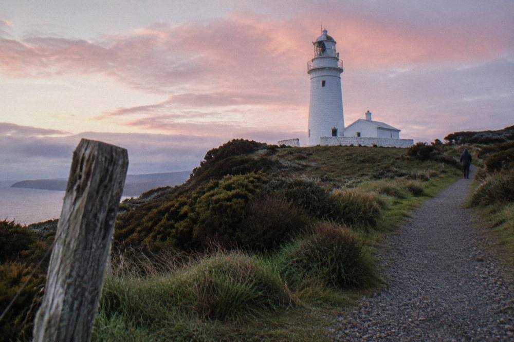 A white lighthouse tower on a green headland above a rocky coastline