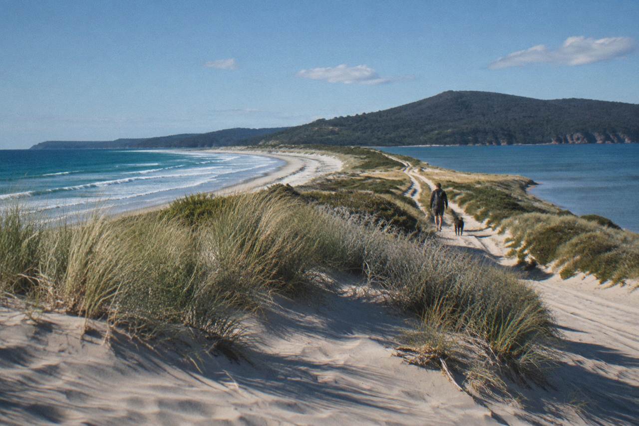 A view over the narrow sandy isthmus connecting north and south Bruny Island under a bright sky