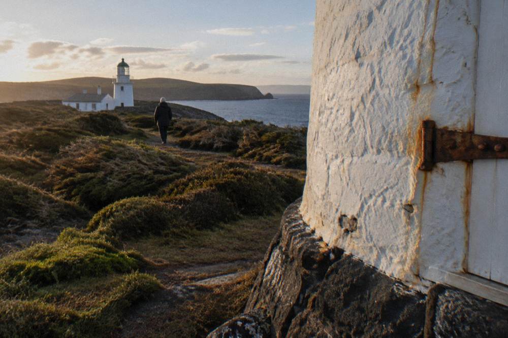 White stone lighthouse on a green headland above a rocky coastline and open sea