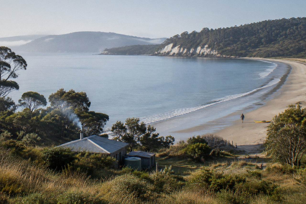 View across calm water to a green island coastline with a sandy beach and low cliffs