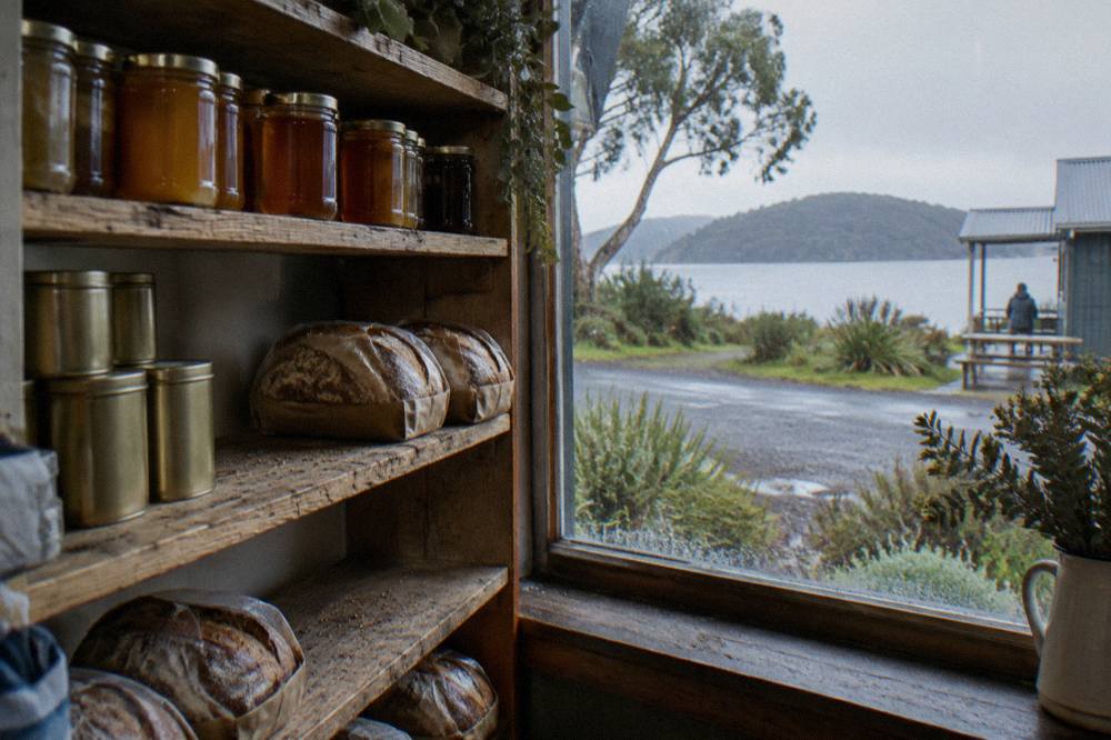 A wooden shelf inside a general store stocked with jars of honey, tins of food, and loaves of bread