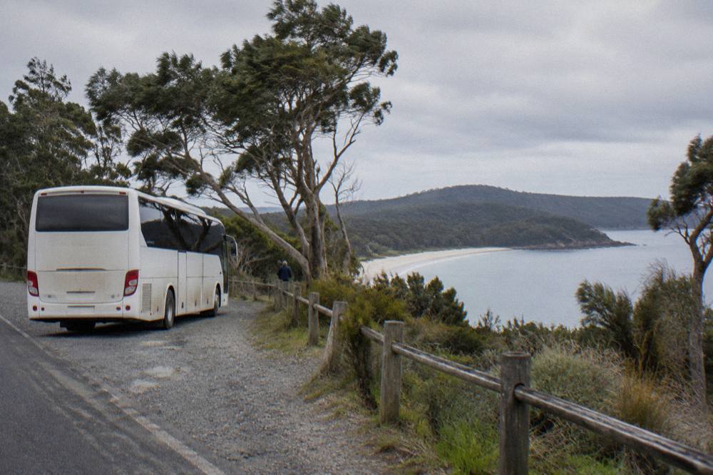 A coach parked beside a coastal road overlooking a sheltered bay