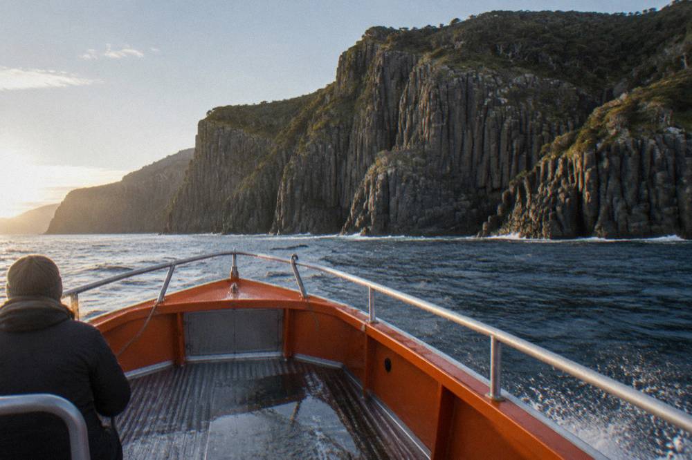 An open cruise boat passing tall sea cliffs above dark water