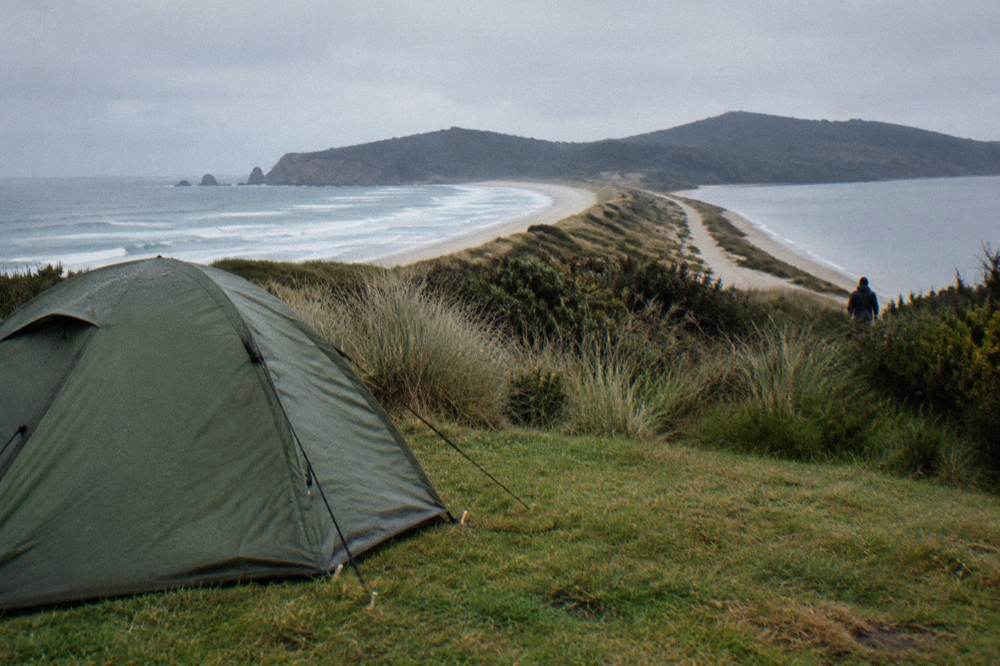 A campsite at The Neck with a tent pitched on grass and a view of the narrow isthmus and ocean beyond
