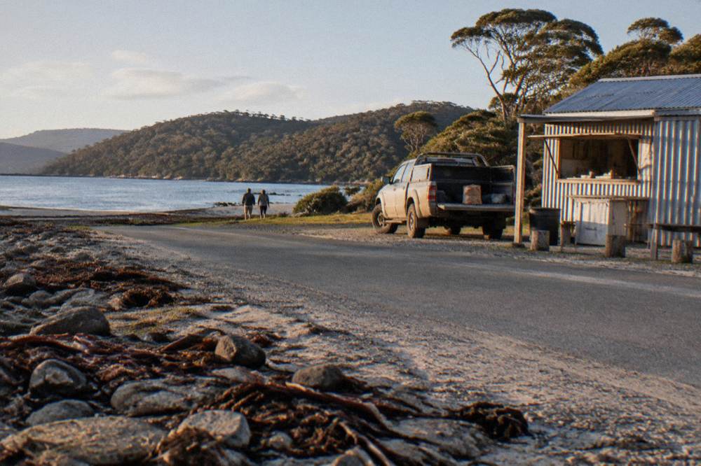 A country road beside a shoreline with a small roadside food shed