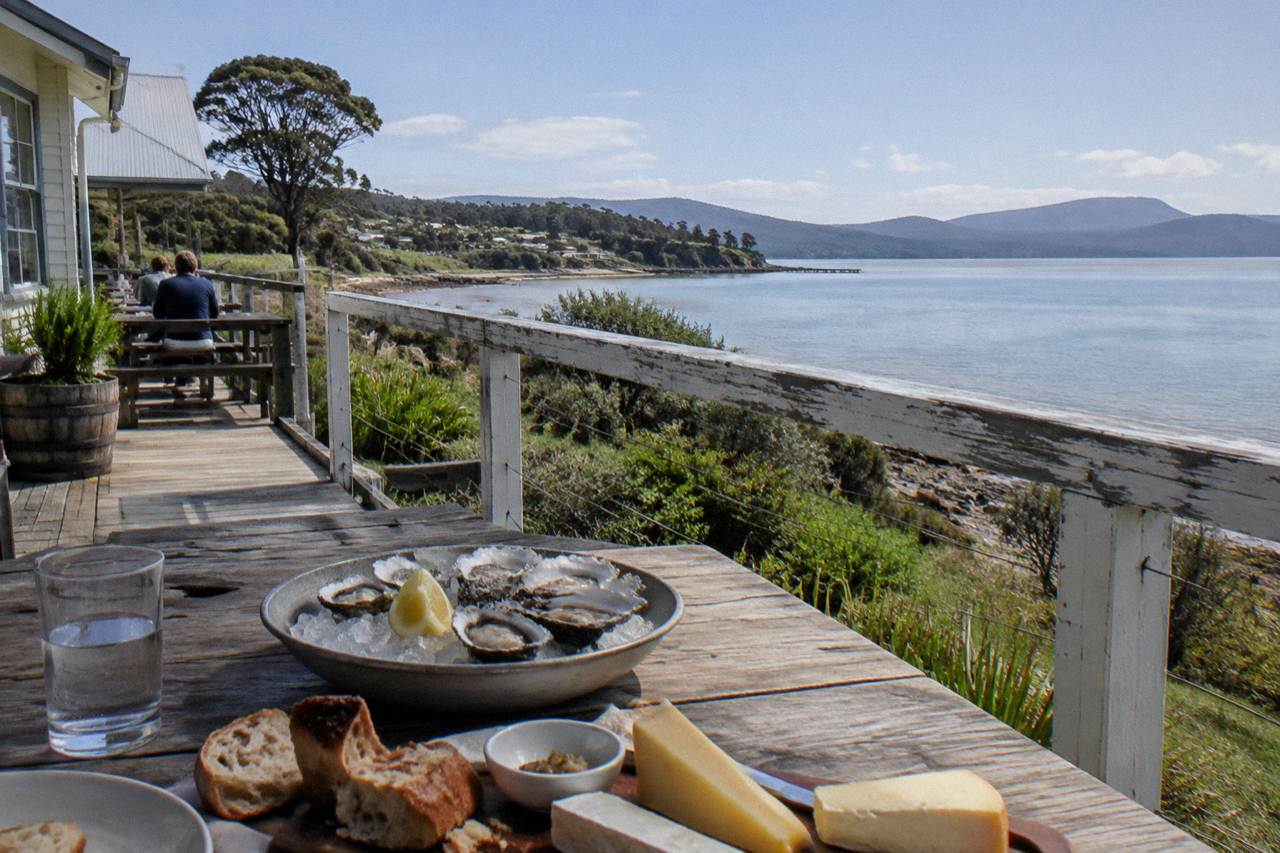 A wooden table with cheese, oysters and bread overlooking a calm bay