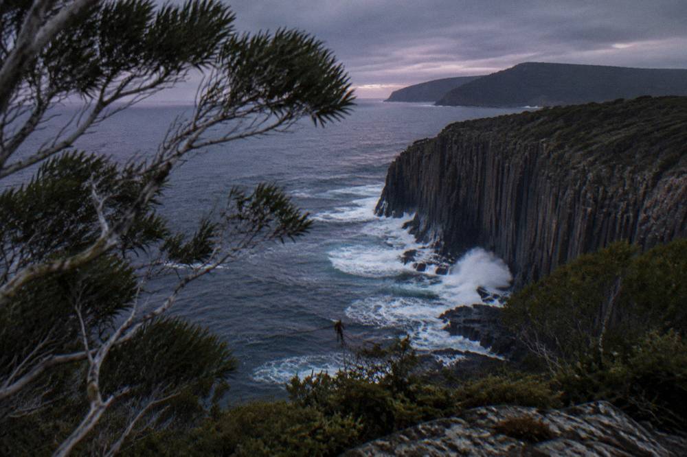Dark ocean swell breaking against steep rock columns at the south end of an island at the end of the day