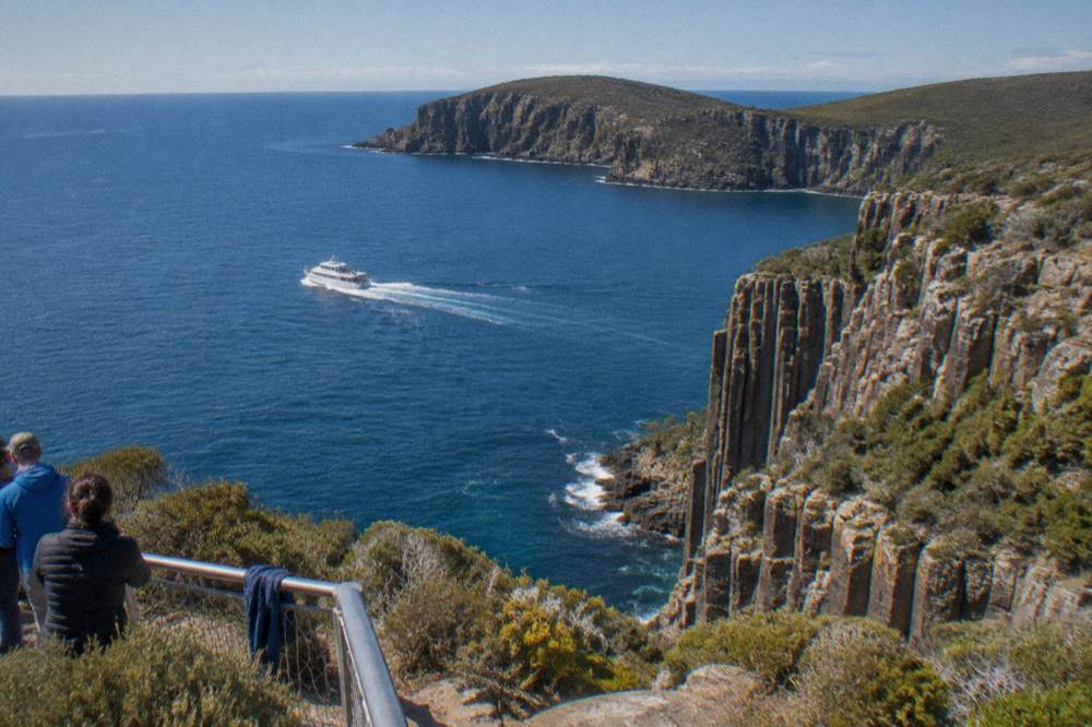 A small boat seen from above between a headland and deep blue open water