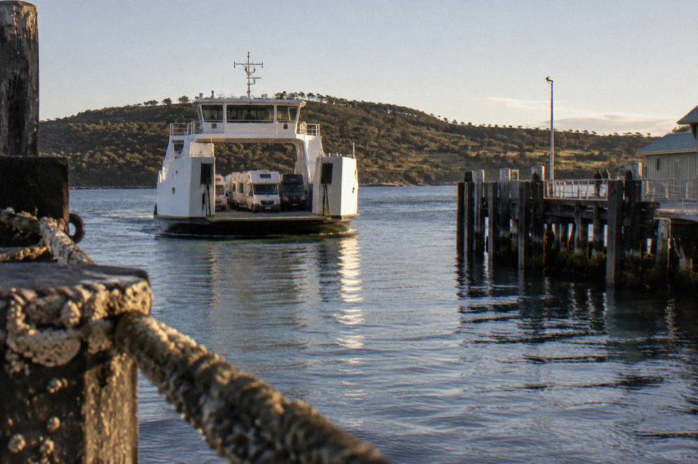 A vehicle ferry approaching a small timber jetty terminal on a sheltered waterway