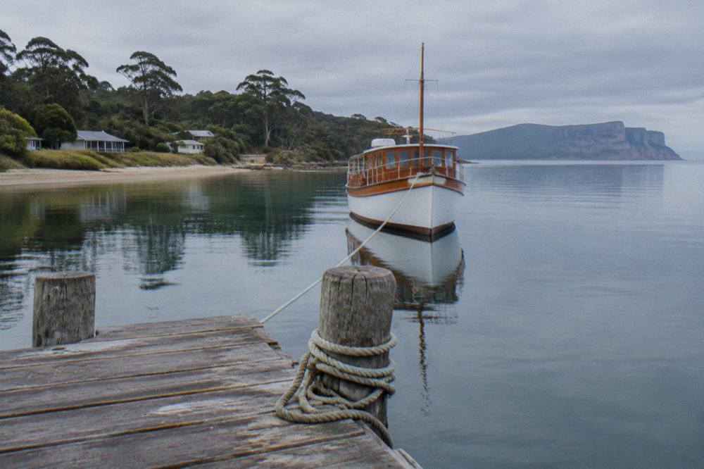 Wooden cruise boat near a jetty on calm water with dolerite cliffs in the distance