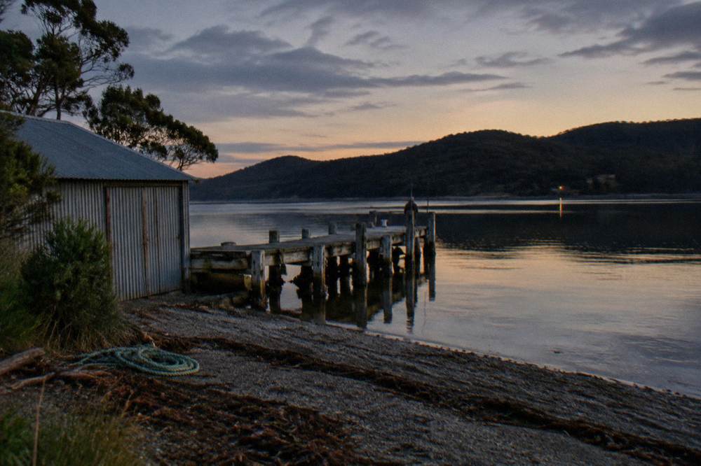 Small jetty over still water at dusk with low hills behind