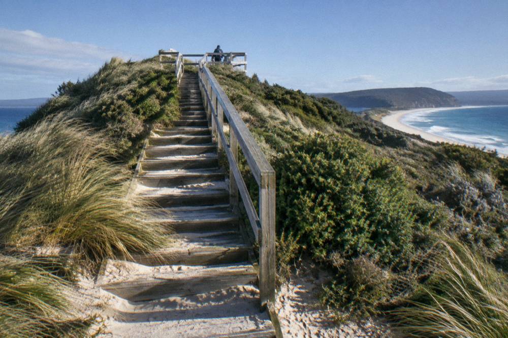 Wooden steps leading up to a viewing platform above a narrow sandy isthmus