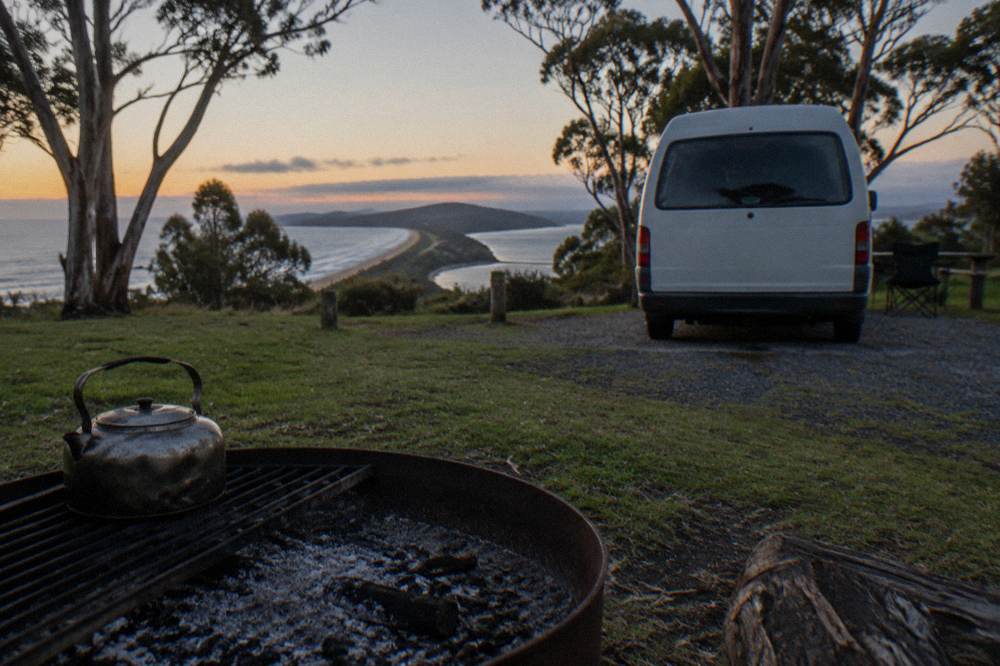 Campervan parked at a grassy site with eucalyptus trees and a fire pit