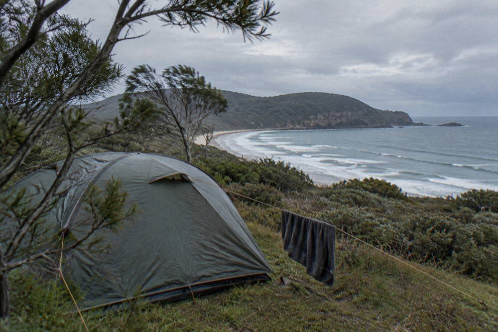 Tent beside a coastal shrubland with grey ocean swell beyond the headland