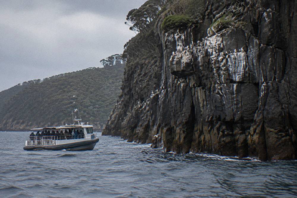 Open cruise boat travelling close to a steep rocky cliff face on open water