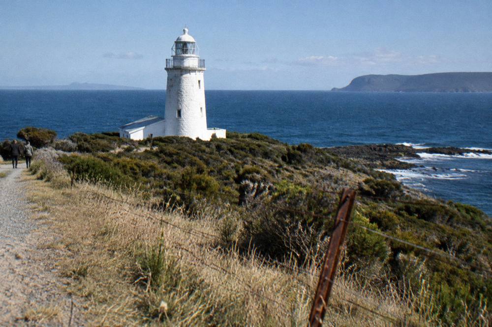 White lighthouse tower on a grassy headland above the sea
