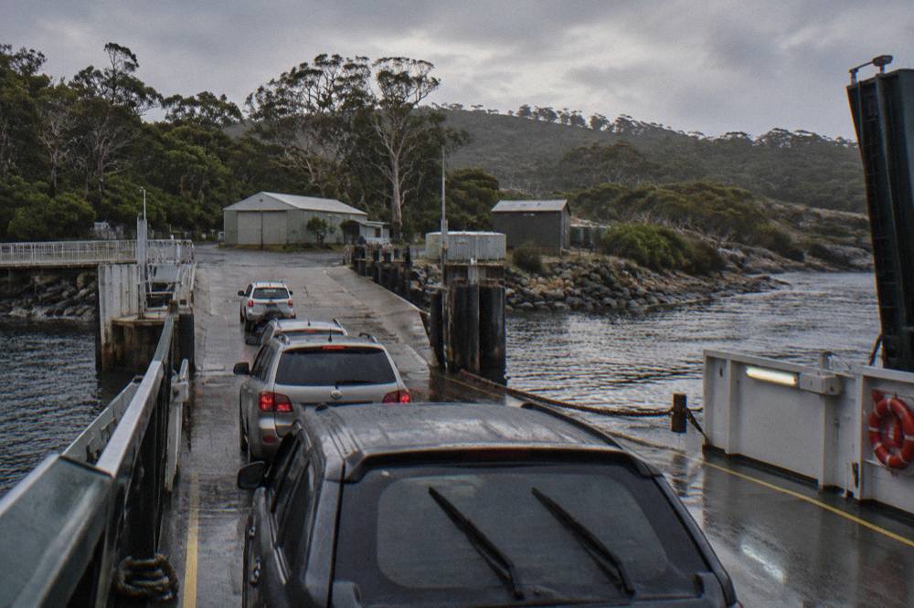 Cars queued on the ramp at a small ferry terminal beside the water