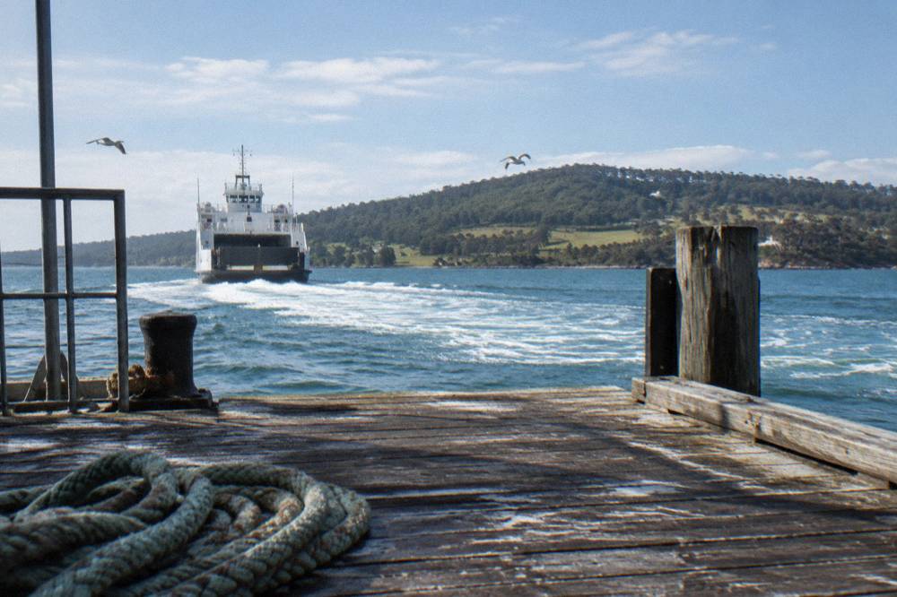 Ferry sailing away from a wooden jetty toward a green island shoreline