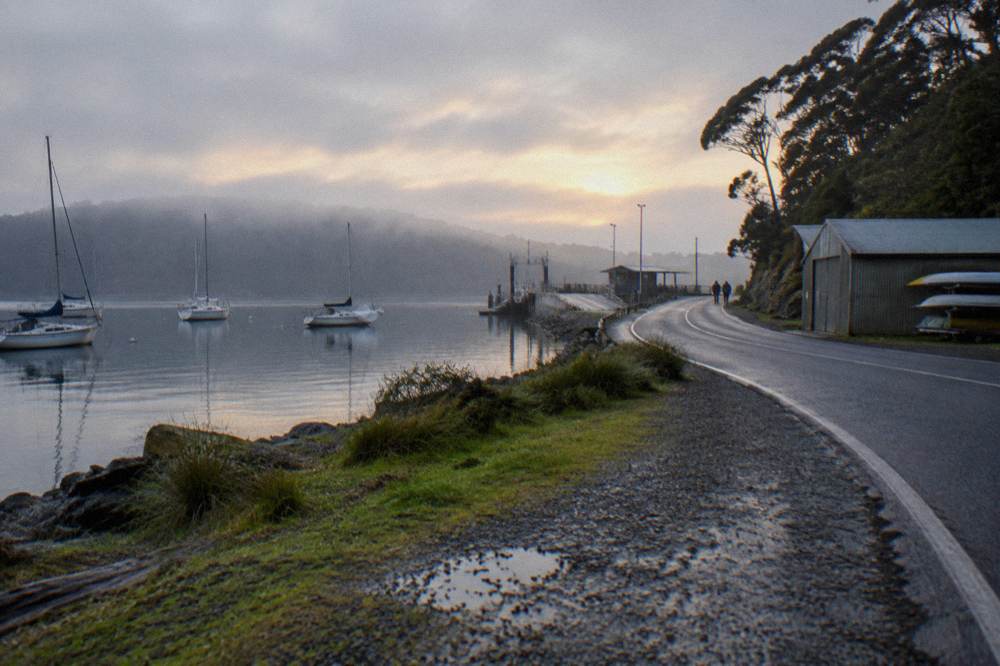 Coastal road winding past a sheltered bay with boats at moorings