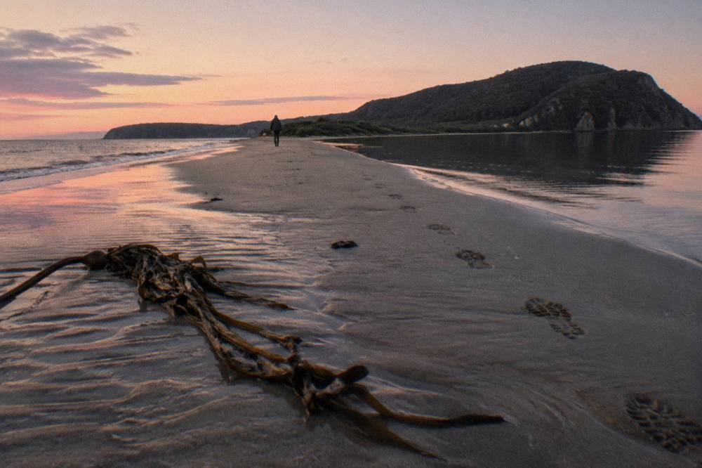 Dusk sky fading over calm water beside a sandy spit with dark headlands beyond