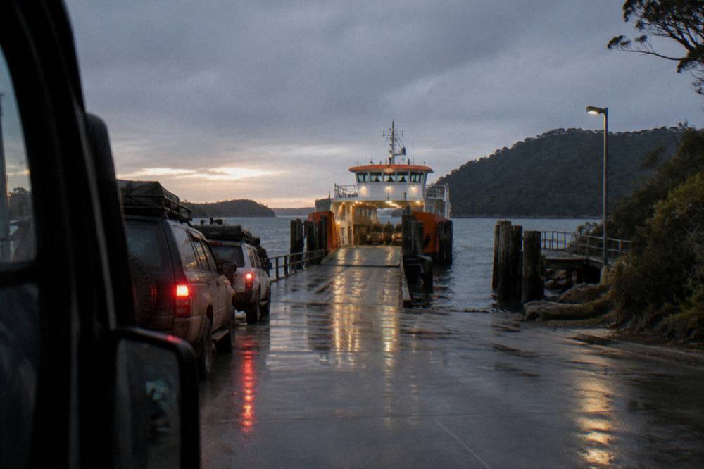 Vehicle ferry approaching a timber ramp at a sheltered terminal at dusk