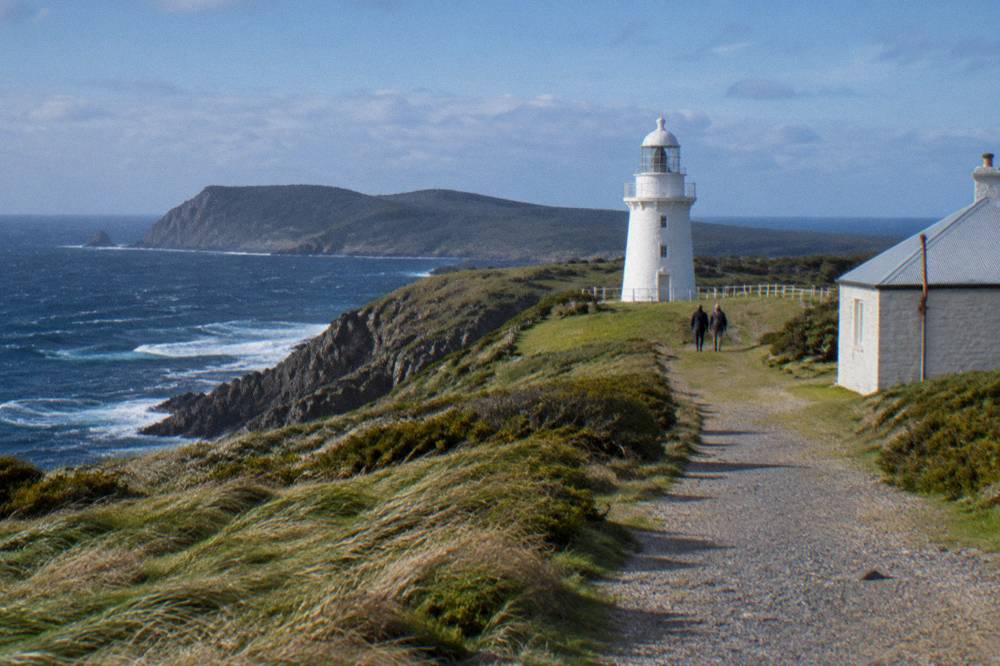 A stone lighthouse standing on a green headland above cliffs and open sea