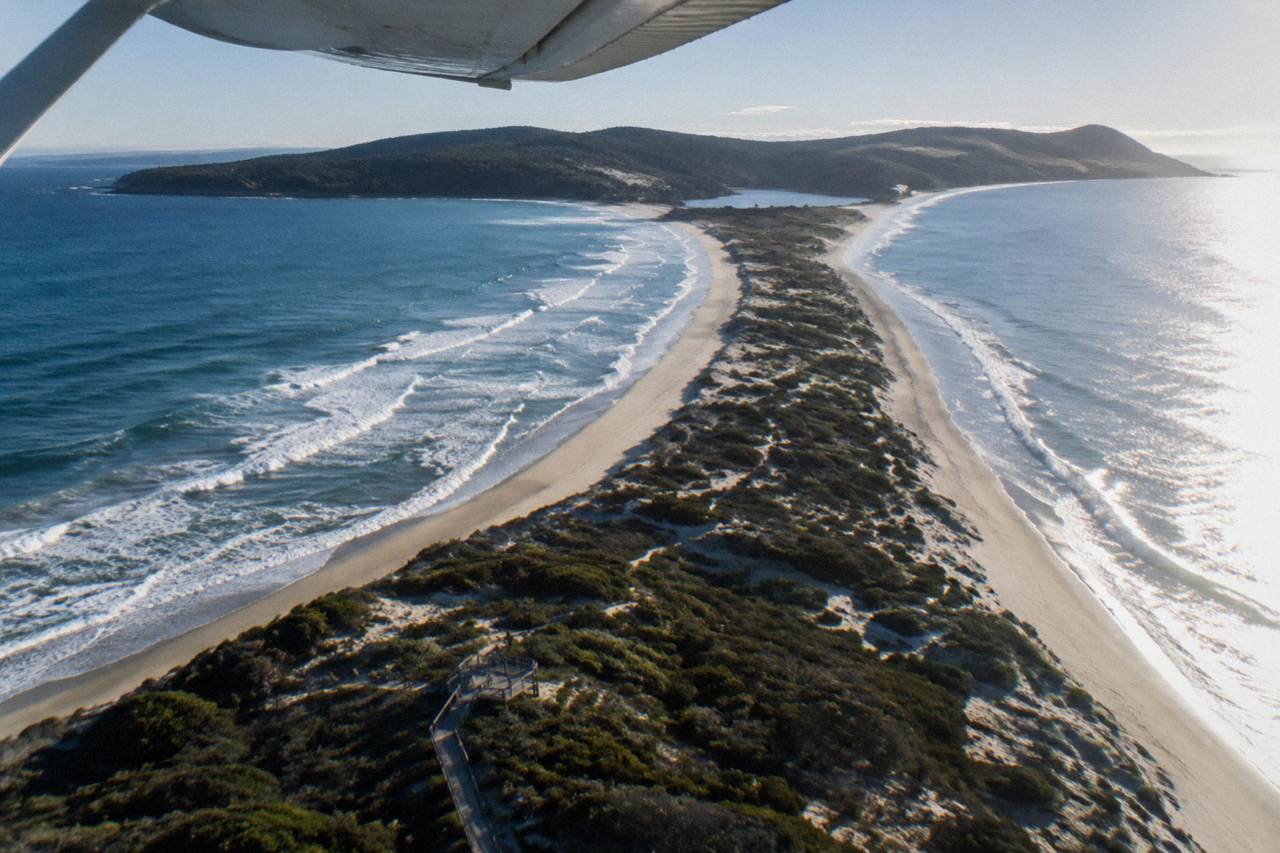 A small light aircraft flying above a green island coastline with white cliffs and blue sea