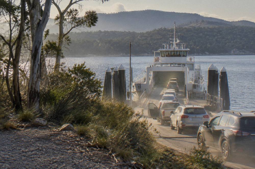 A vehicle ferry loading cars at a sheltered jetty terminal with forested hills behind