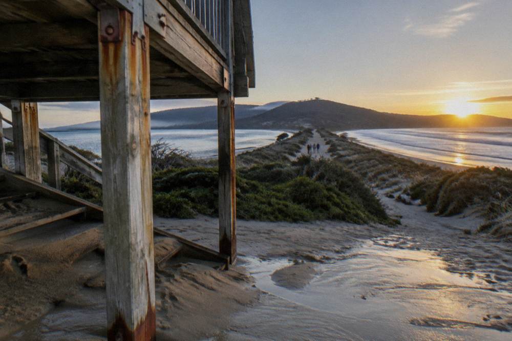 A wooden viewing platform above a narrow sandy isthmus joining two halves of an island