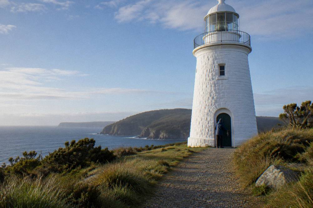 A guide unlocking the door of a white stone lighthouse on a grassy headland