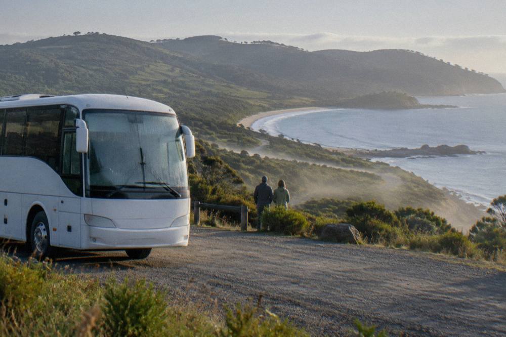 A coach parked near a lookout above the coastline of South Bruny Island with green hills behind