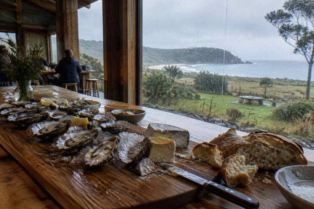 A platter of cheese, oysters and bread on a wooden table at an island cellar door