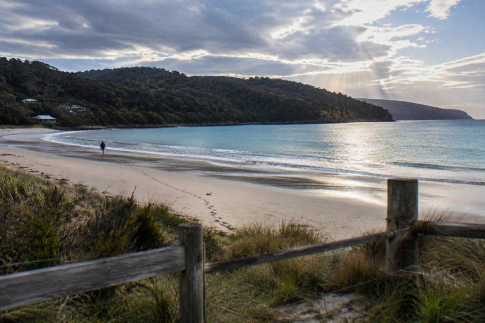 Sunlight breaking through clouds over calm blue water at Adventure Bay with a sandy beach