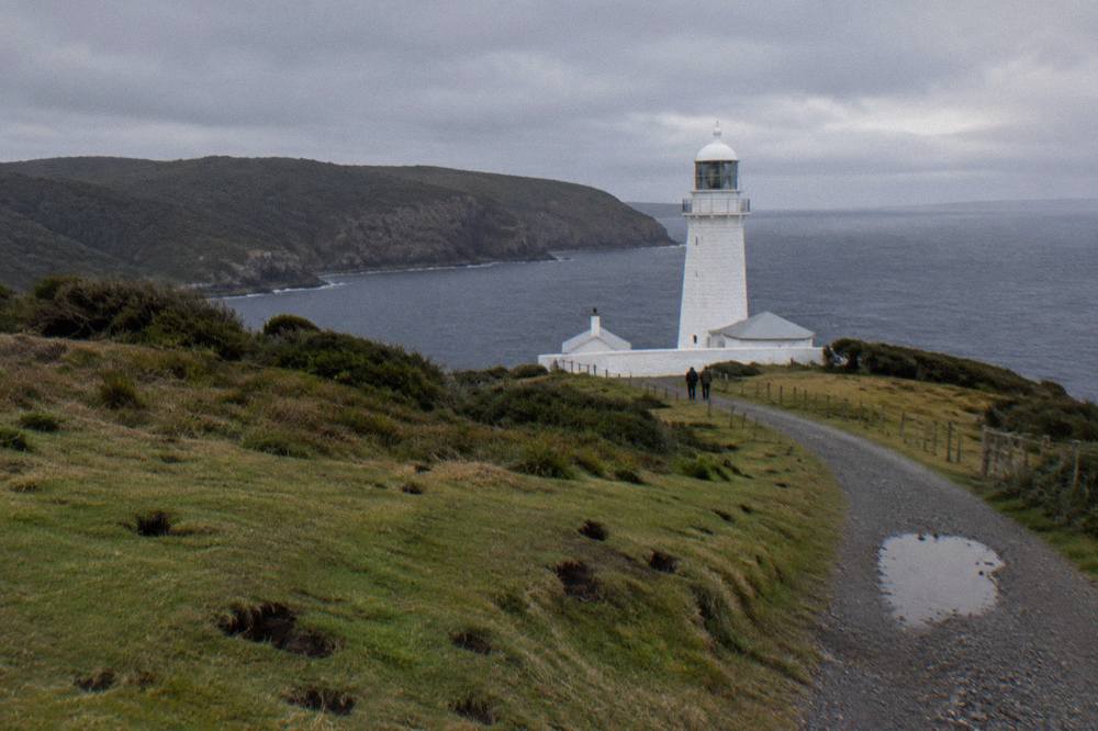 Stone lighthouse tower beside a gravel path on a grassy headland at Cape Bruny