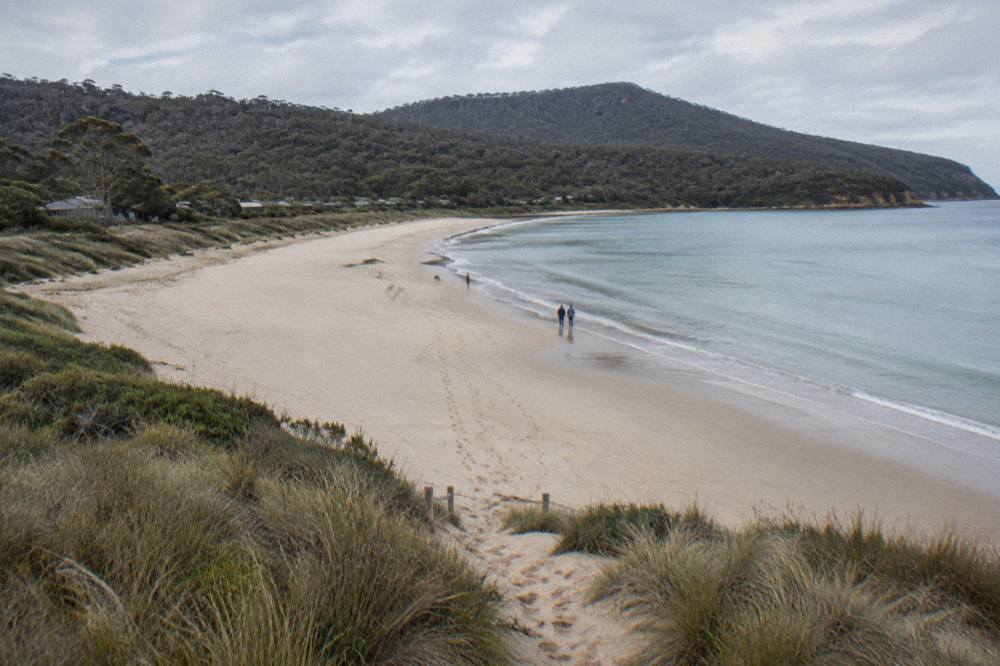 Curving white sand beach with calm shallows and forested hills behind