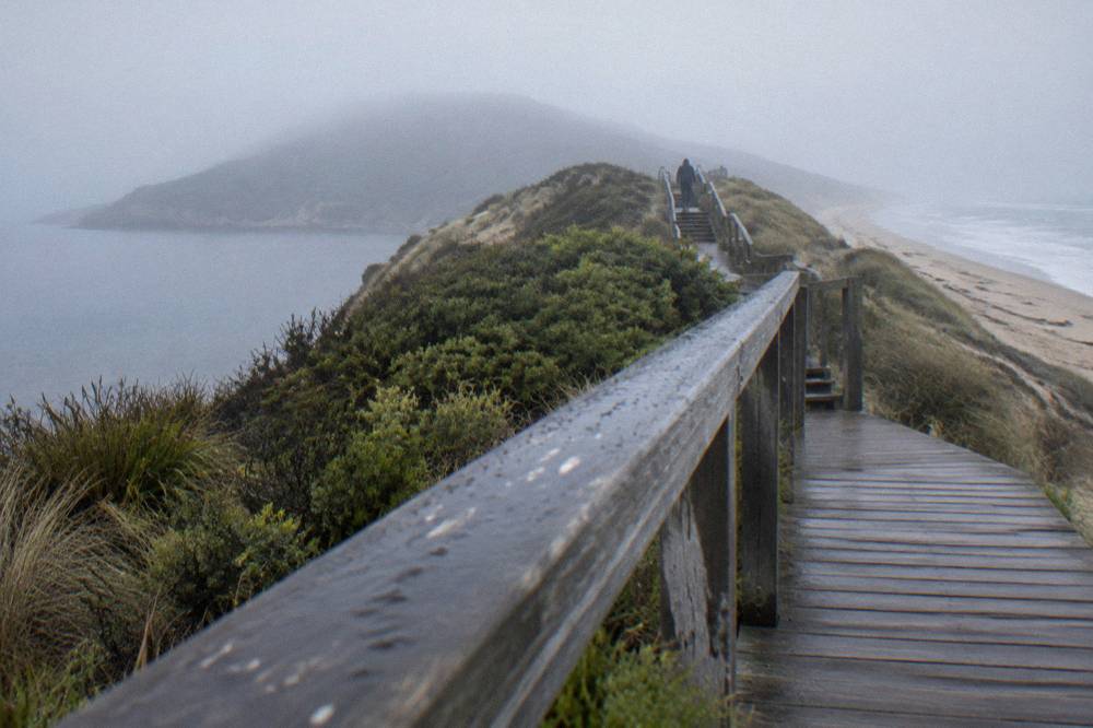 Timber viewing platform and boardwalk rising over low dunes toward a narrow sandy isthmus