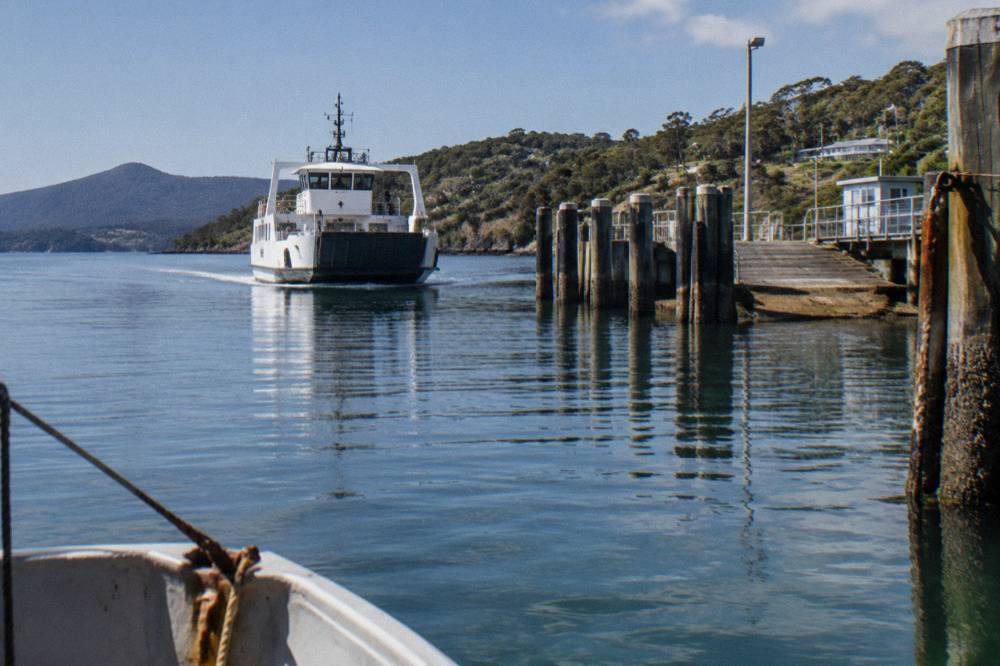 A vehicle ferry approaching a timber ramp jetty across calm water
